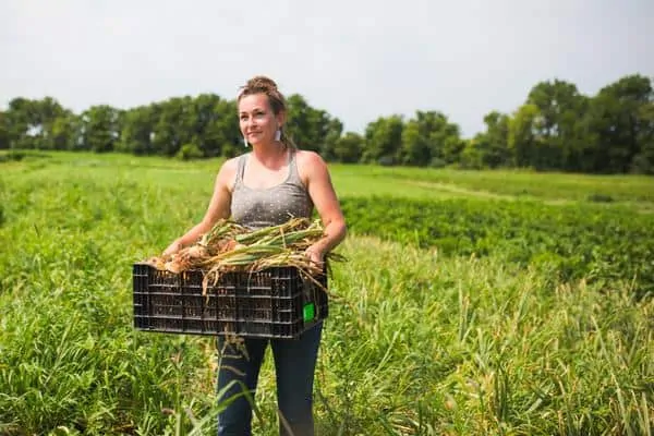 Lauren Rudersdorf, a millennial farmer carries crops through a field 