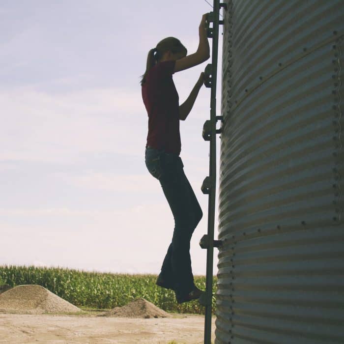 Marji Alaniz climbing a grain bin ladder with corn in the background.