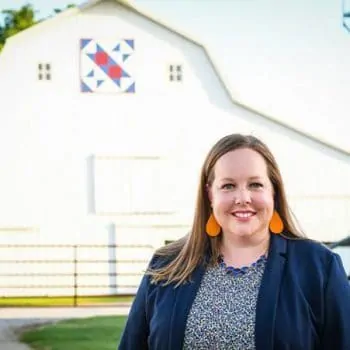 Erin Cumings balances a career at Nationwide with life on the farm. Here she stands on the farm in front of a white barn.