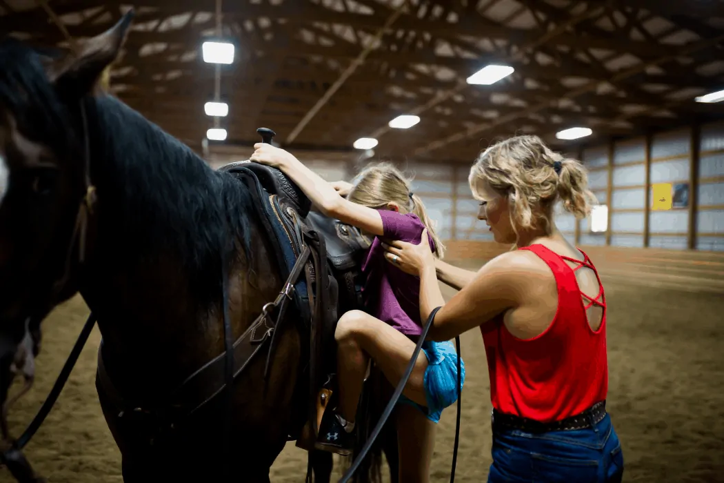 Sarah Eberspacher helps a student up on a horse for lessons. 