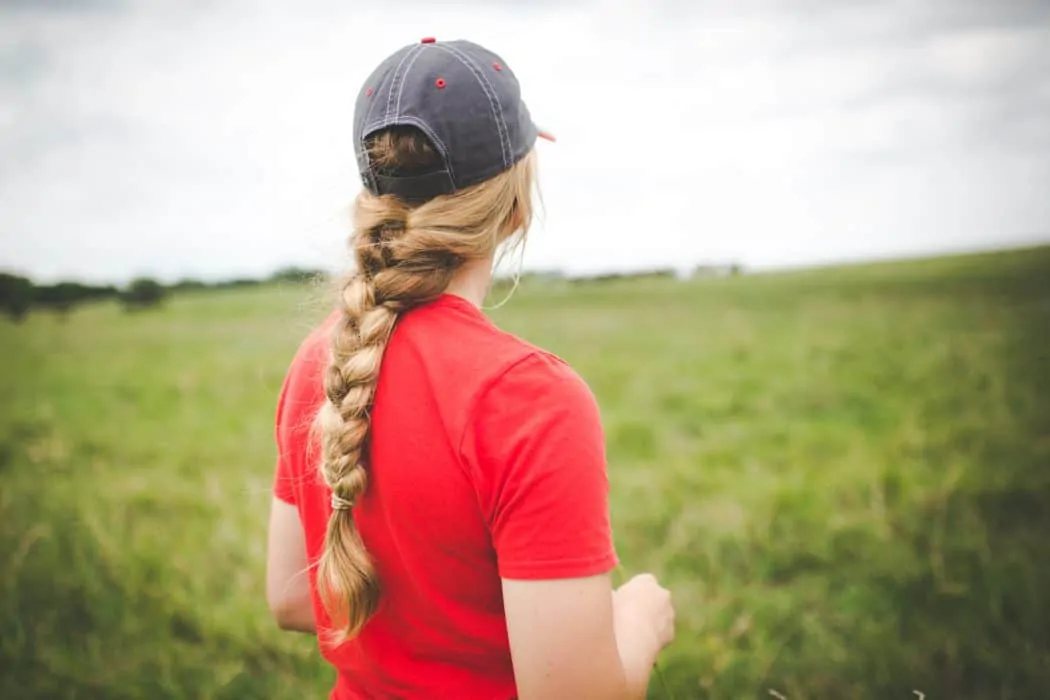 Woman with braid and hat in red tee shirt standing in field on Nebraska farm.