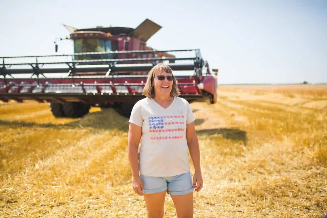 Woman standing in a freshly cut wheat field in front of a a CASE combine in a patriotic shirt. 