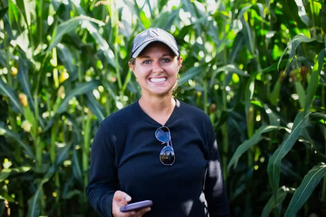 Woman farmer standing in corn field in Nebraska with phone in her hand.