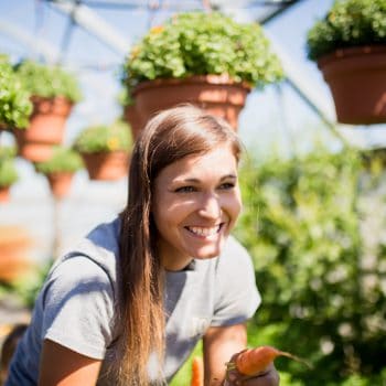 Woman smiling and standing in greenhouse where fresh produce is grown.