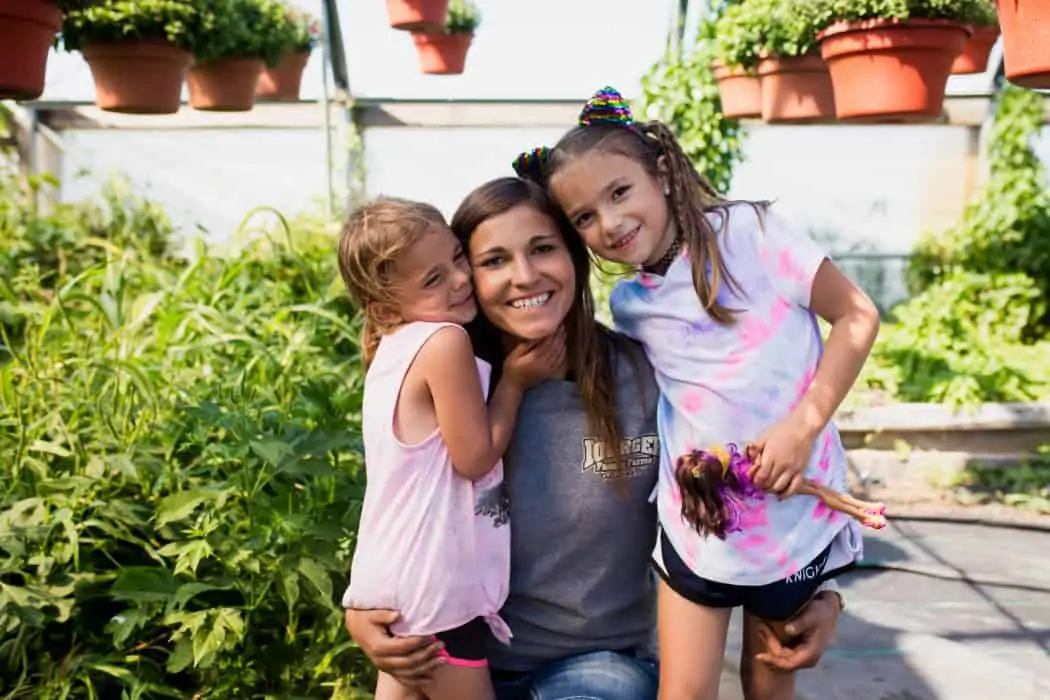 Woman hugging two young girls who are her family members in a greenhouse. 
