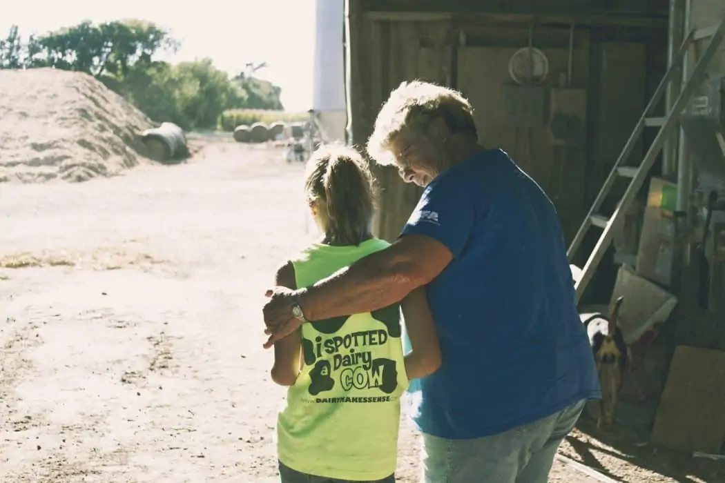 Older woman hugging and giving advice to younger girl on the farm in a barn. 
