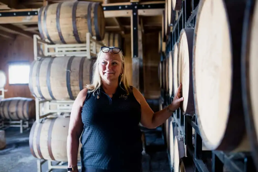 Liz Henry standing next to barrels of bourbon at J. Henry & Sons bourbon farm.