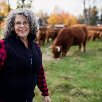 Janet Stewart of Greenfield Highland Cattle standing in a field with her cattle in Vermont.