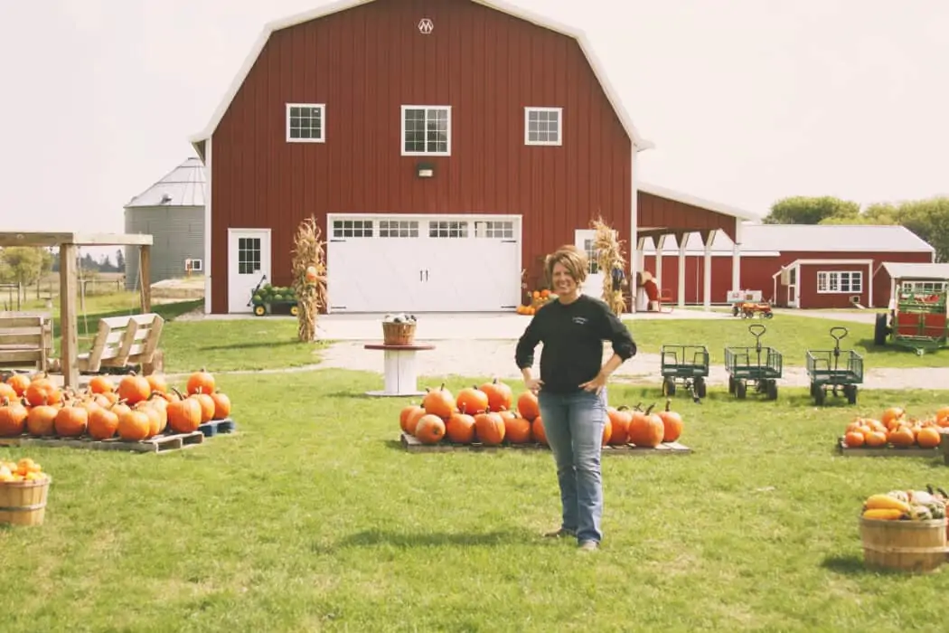 Shannon Latham, owner of Enchanted Acres, standing in front of her barn and pumpkins.