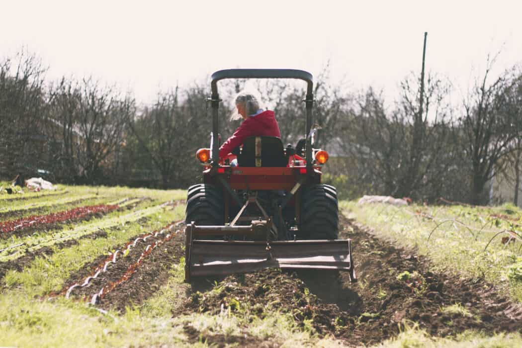 A woman in a red jacket driving a tractor through a produce field. 