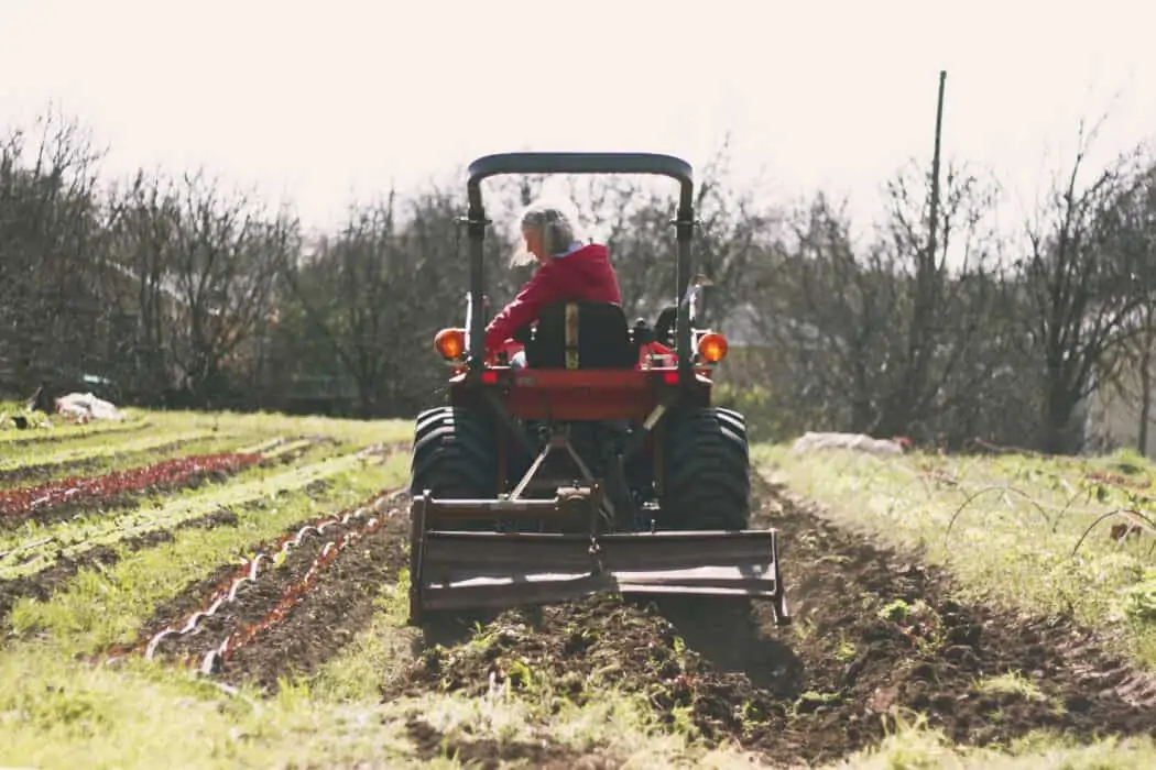 A woman in a red jacket driving a tractor through a produce field. 