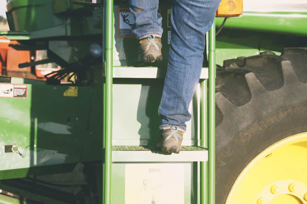 Boots climbing up a ladder of a John Deere combine