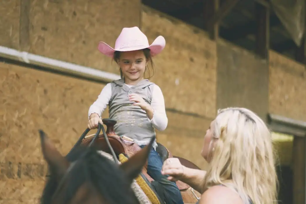 Young girl with pink cowgirl hat riding a horse during her horseback riding lesson
