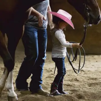 A young girl leading her horse with help from her teacher