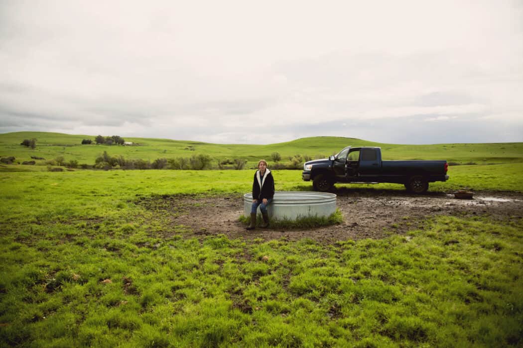 RanchHer sitting on a water tank in a pasture next to her blue Dodge Ram pickup truck