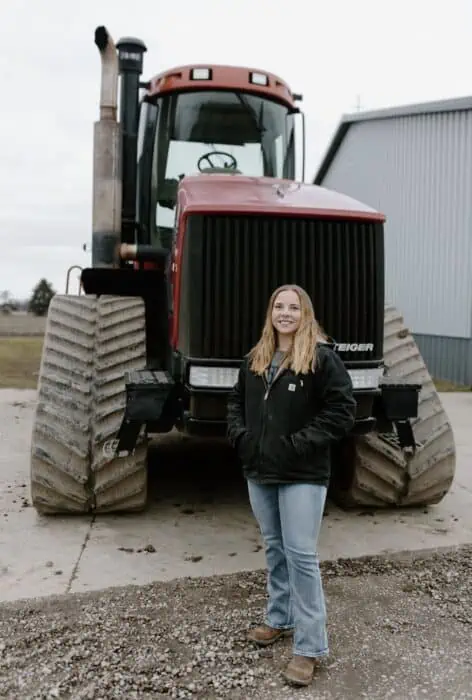 Blonde woman standing in front of a tractor