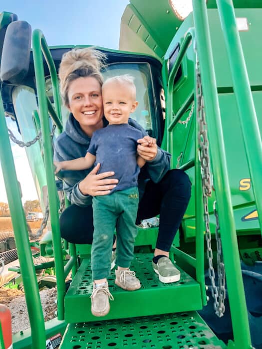 Farm mama Chelsey stands with her son on a John Deere combine