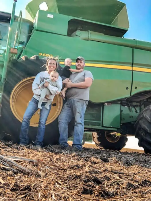 Family holding there children next to a John Deere combine on the farm