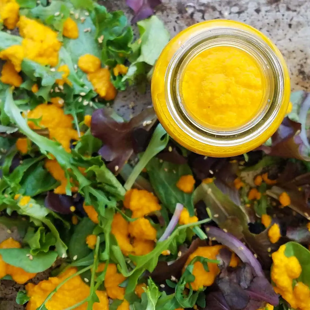 an overhead view of carrot and ginger salad dressing surrounded by salad greens and other bits of dressing.